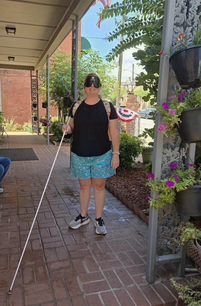 Lindsey wearing shades and using a white cane outside the Louisiana Center for the Blind in the summer of 2026.